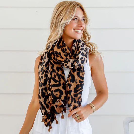 Woman wearing a leopard print scarf and white outfit against a light background