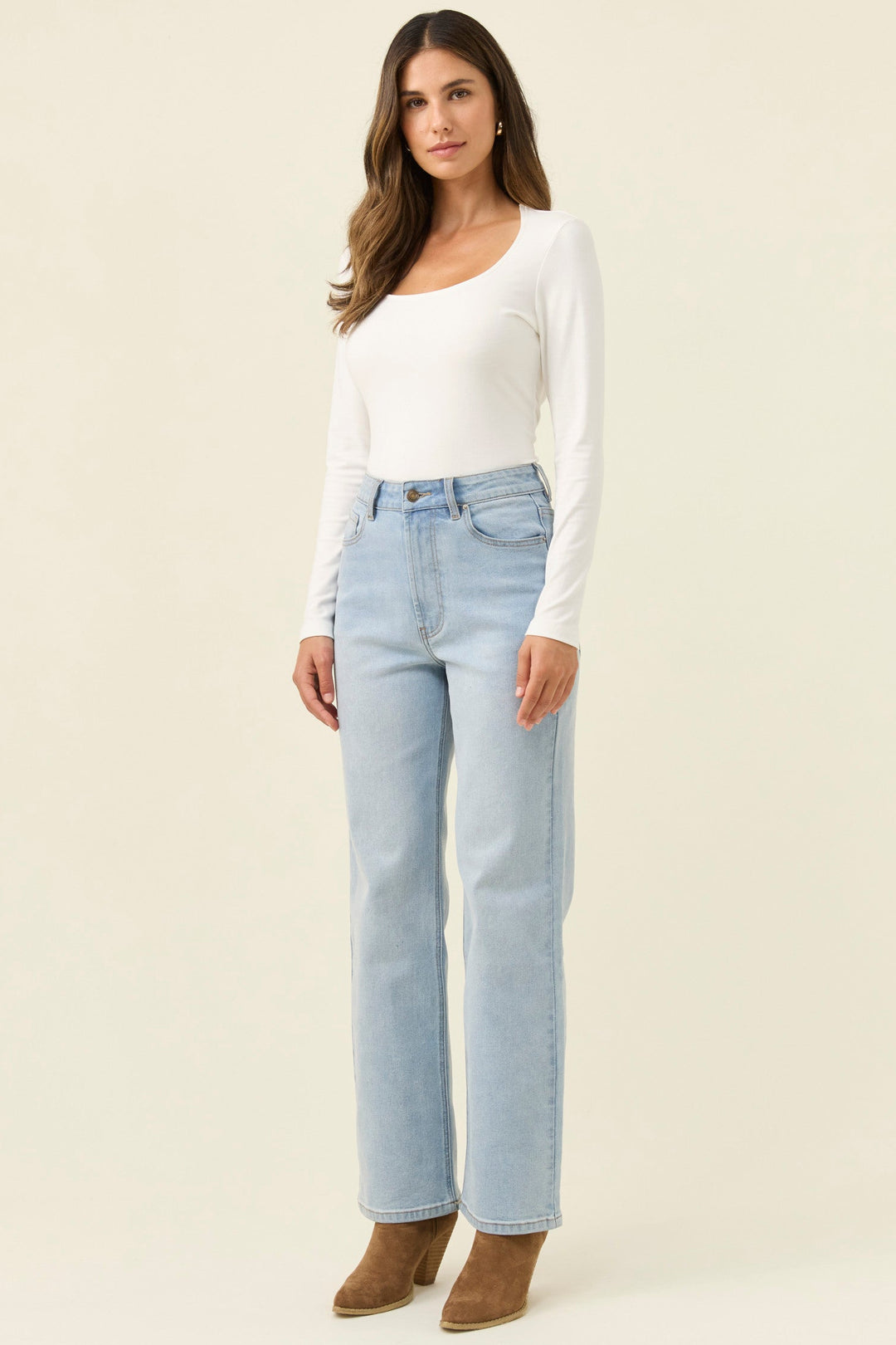 Woman wearing a white long-sleeve top and light blue jeans on a beige background