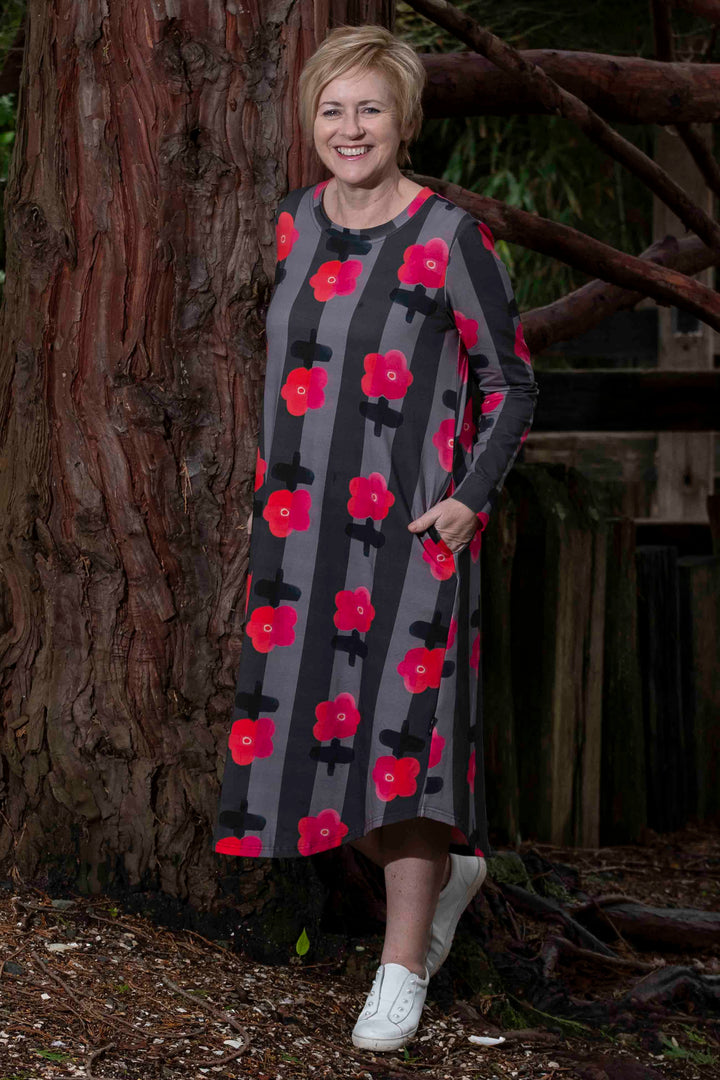 lady wearing a fun striped and pink flower dress standign by a tree