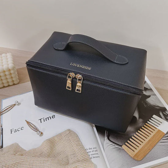 navy travel cosmetic case with gold accents on a magazine with a comb and towel