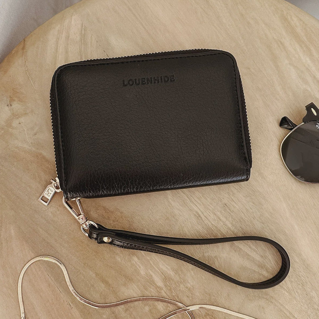 Black wristlet louenhide wallet with a visible brand logo on a wooden surface.