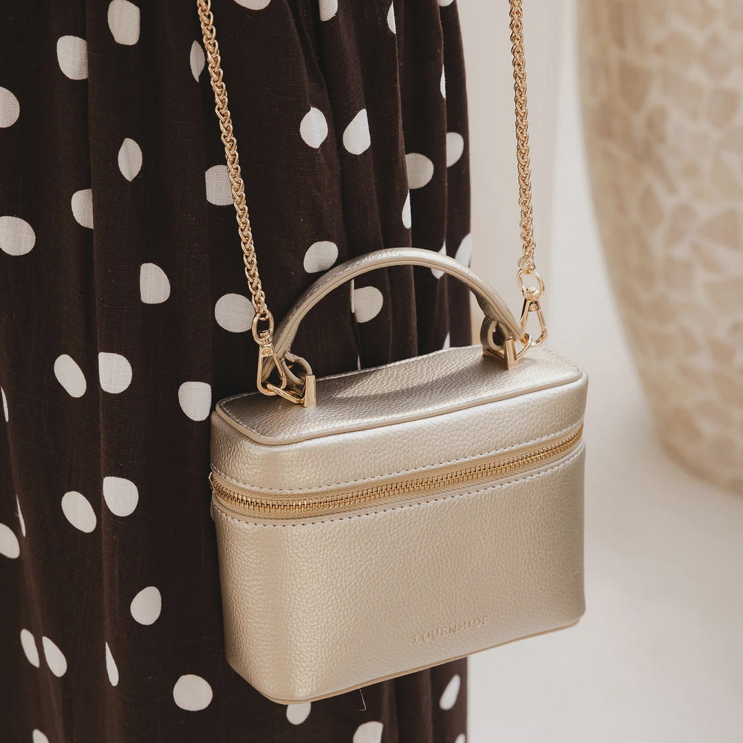 Gold louenhide handbag with a chain strap worn by a person in a polka dot dress.