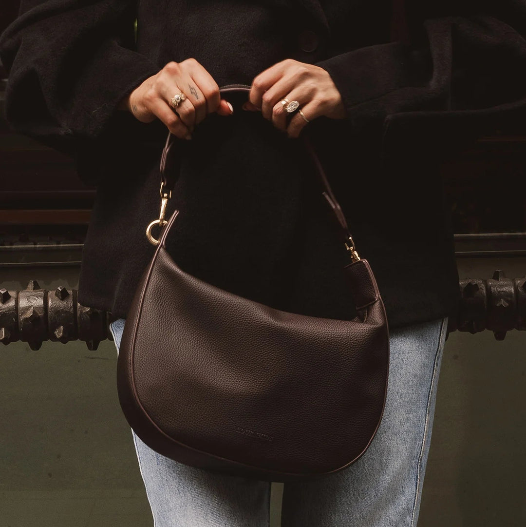 Person holding a brown leather handbag with a dark background