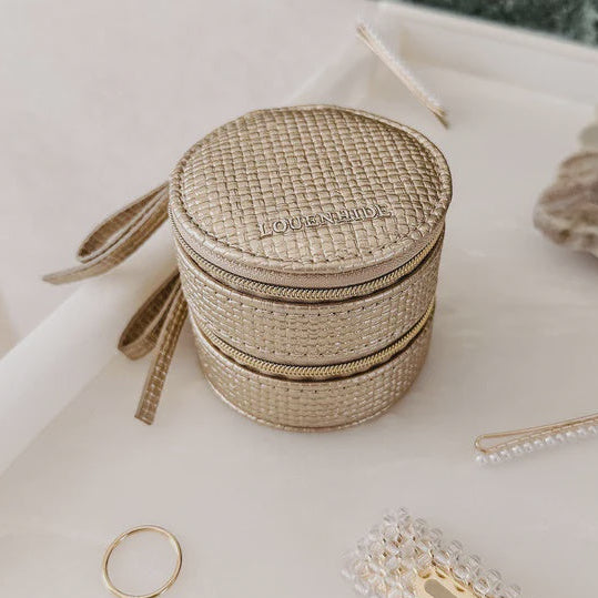 Round woven jewelry box with a gold ring and hair clip on a marble surface