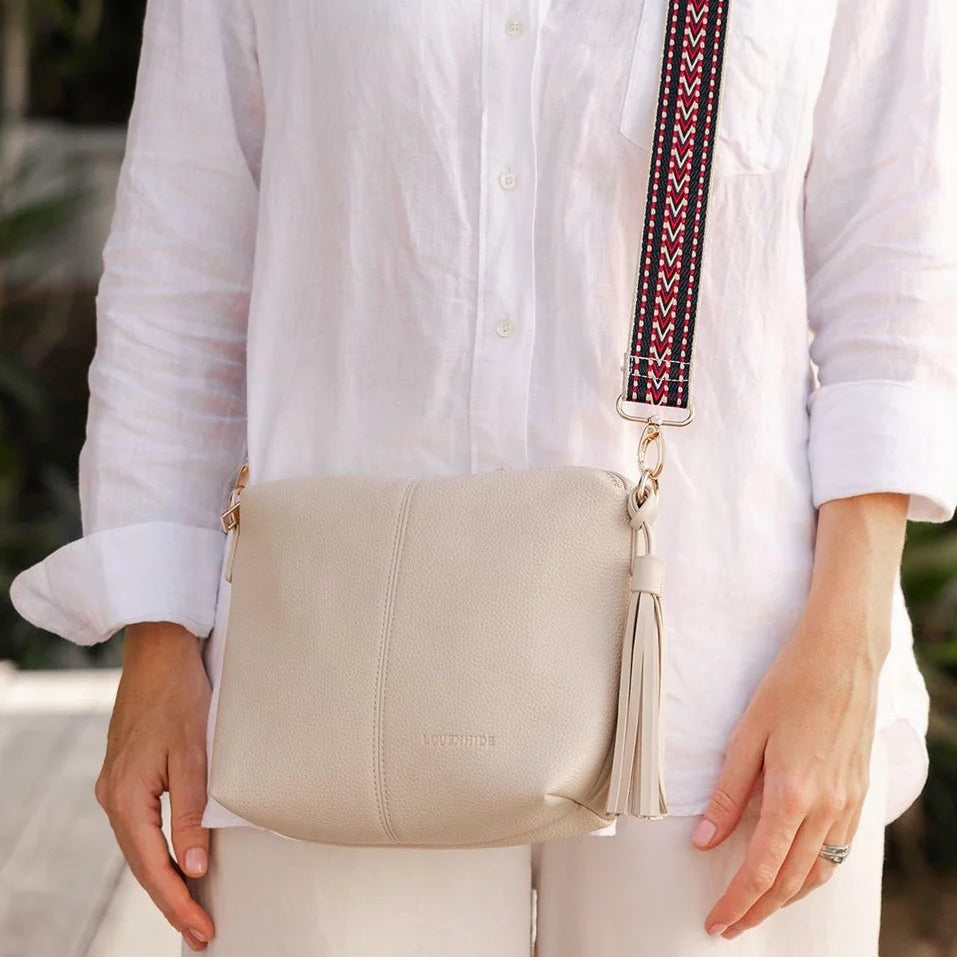 womean in white shirt wearin ga louenhide kasey bag in a light linen colour with a patterned guitar strap.