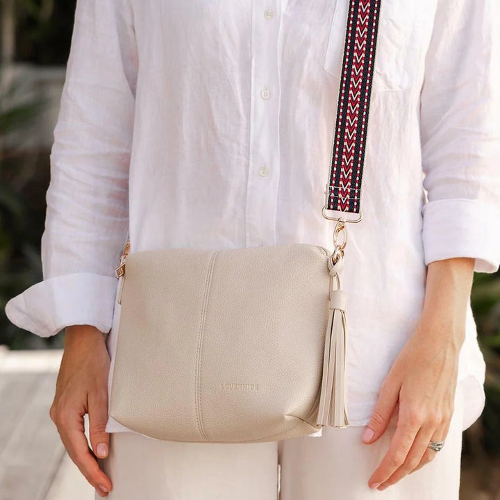 womean in white shirt wearin ga louenhide kasey bag in a light linen colour with a patterned guitar strap.