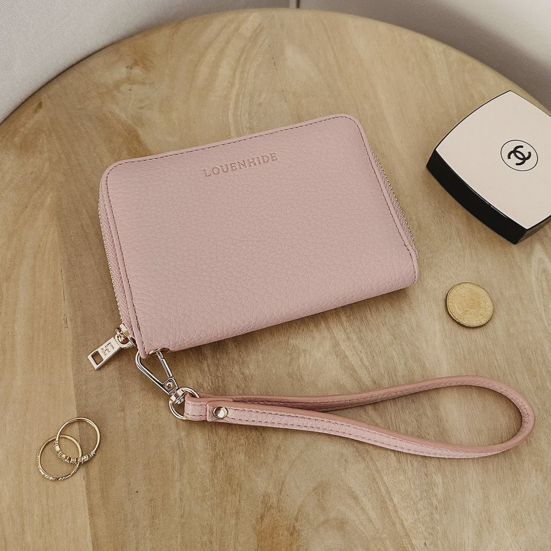 Pink wallet with wrist strap on a wooden surface, next to a Chanel wallet and coins.