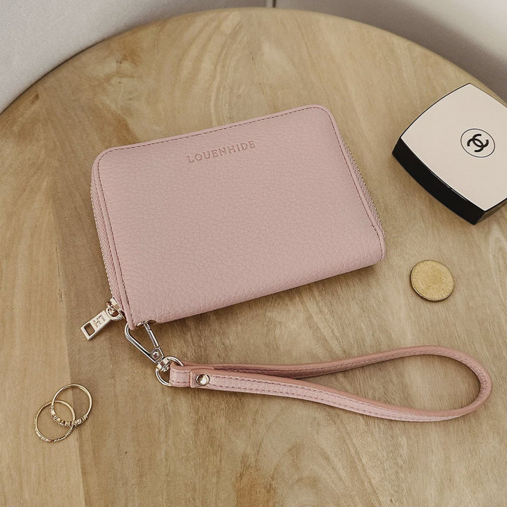 Pink wallet with wrist strap on a wooden surface, next to a Chanel wallet and coins.