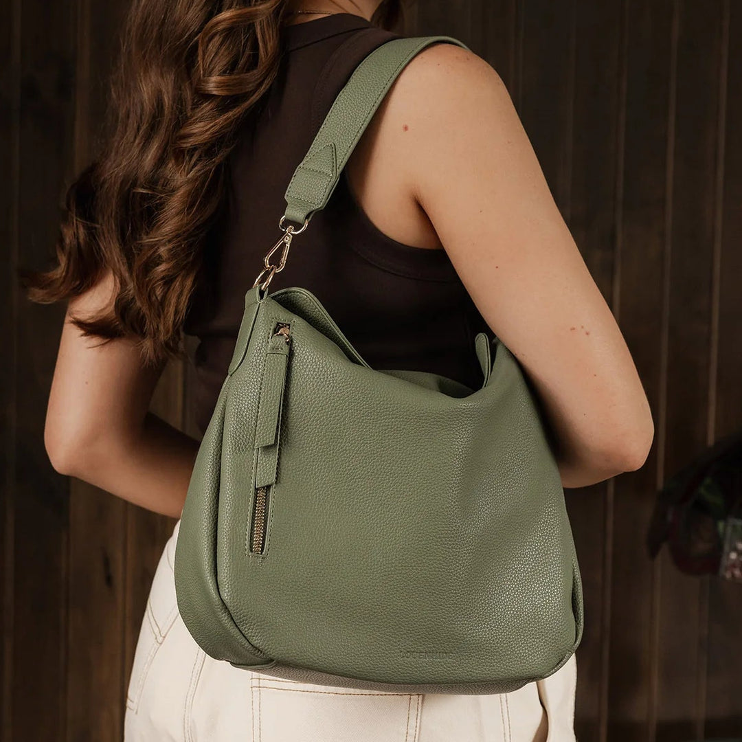 Woman carrying a green louenhide handbag against a wooden background