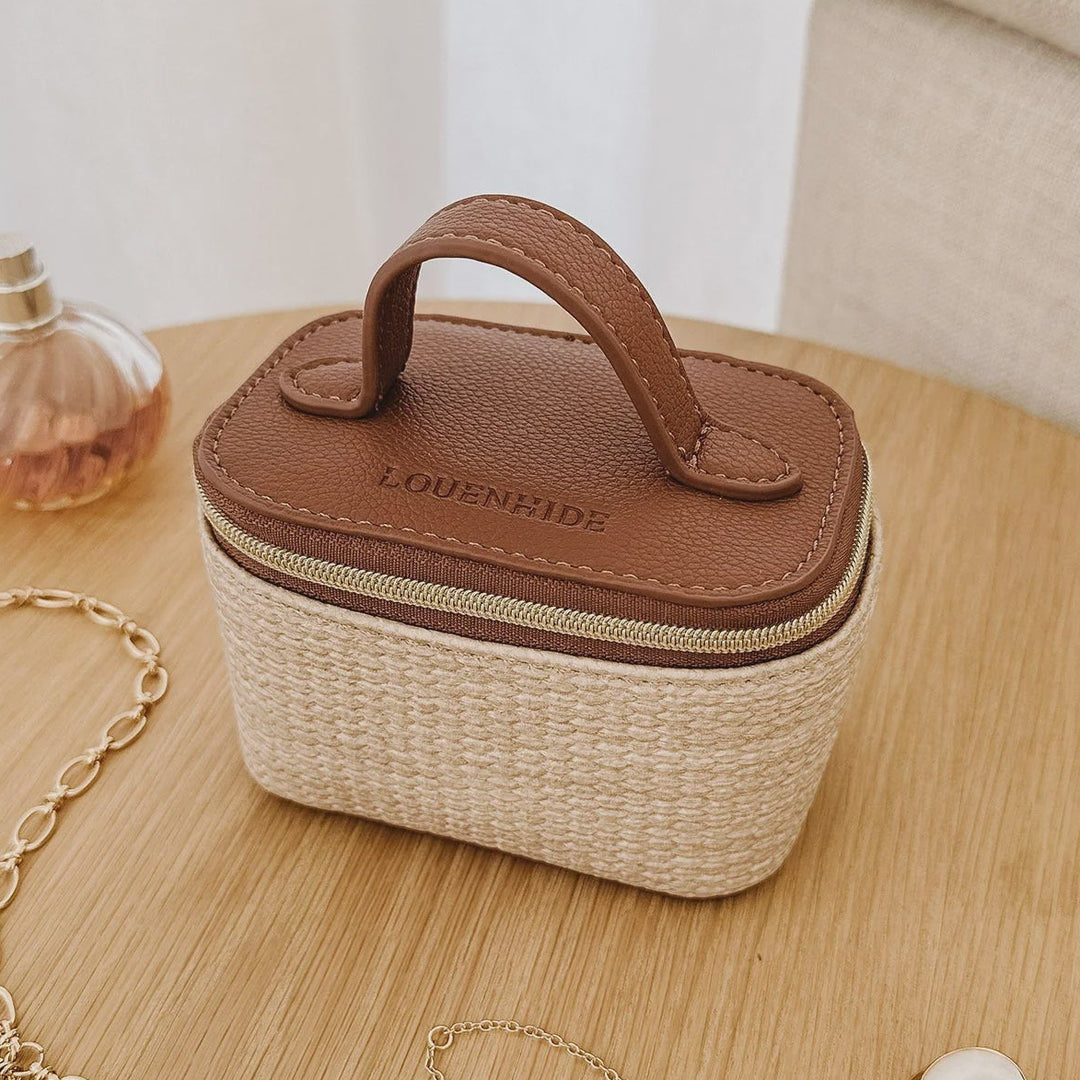 Small louenhide jewelry box with a handle on a wooden surface, surrounded by jewelry items.