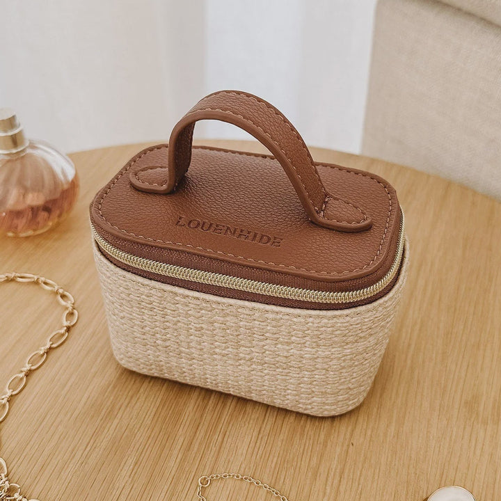 Small louenhide jewelry box with a handle on a wooden surface, surrounded by jewelry items.