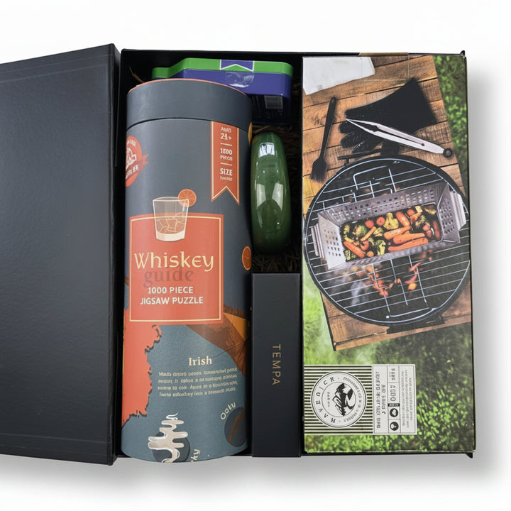 A whiskey guide 1000-piece jigsaw puzzle gift set in its open packaging, featuring a dark gray cylindrical puzzle container with an Irish map design, a green bottle opener, and a printed box cover showing a barbecue scene.