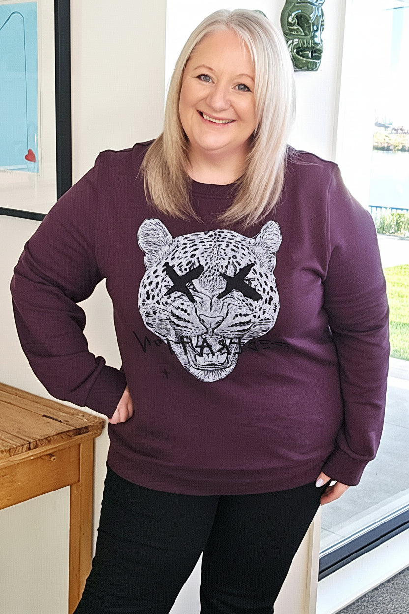 Woman wearing a purple sweatshirt with a graphic design, standing indoors.