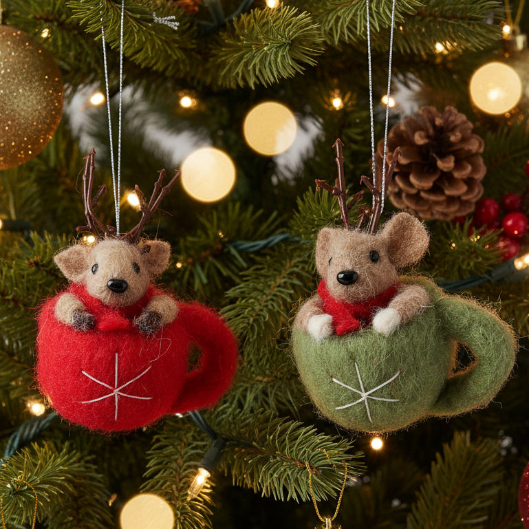 Two felt wool Christmas ornaments shaped like small brown mice sitting in red and green teacups, each with twig antlers and a red scarf, hanging against a CHRISTMAS TREE