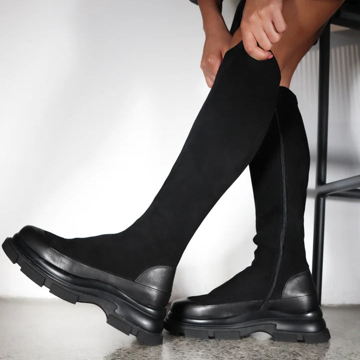 Person wearing black knee-high boots on a light background