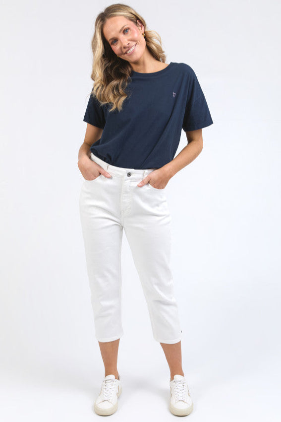 Woman wearing a navy blue t-shirt and white ELM mollie capri pants on a white background