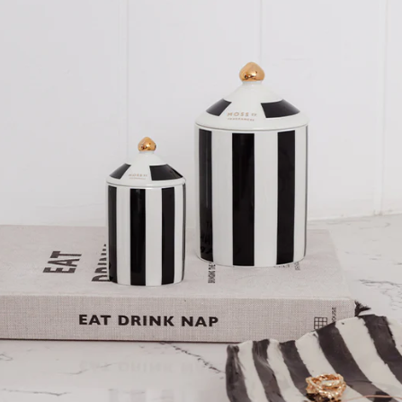 Black and white striped moss st candles on books with a towel and jewellery on a light wooden surface.
