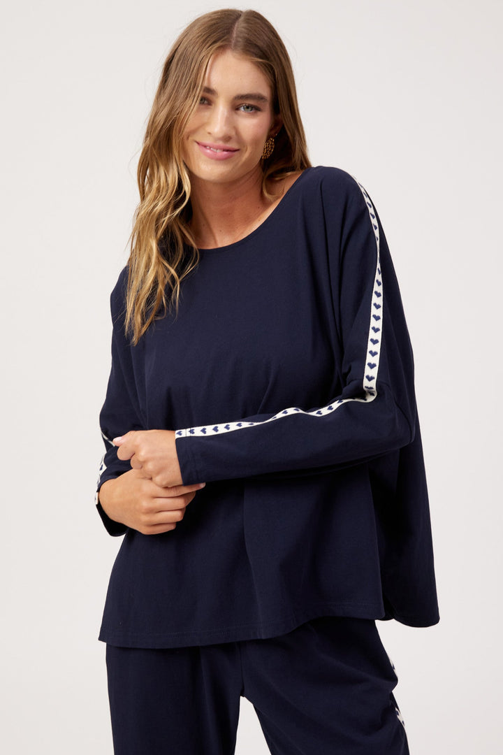 A woman modeling a navy blue long-sleeve top with white patterned stripe details down the sleeves, paired with matching navy pants, against a plain light gray studio background.