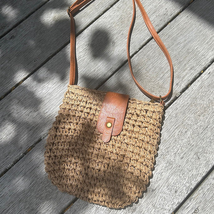 Woven bag with brown leather strap on a wooden surface