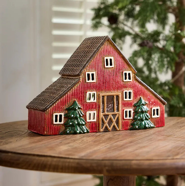 Red barn figurine with green trees on a wooden surface
