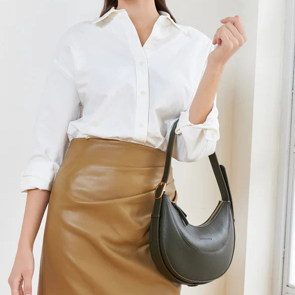 Woman holding a black handbag wearing a white shirt and brown skirt indoors.