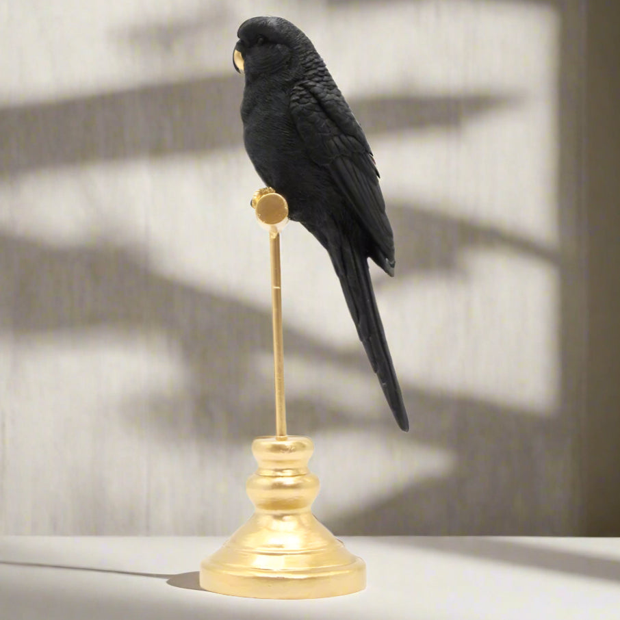 Black bird parrot figurine ornament on a gold pedestal against a white background