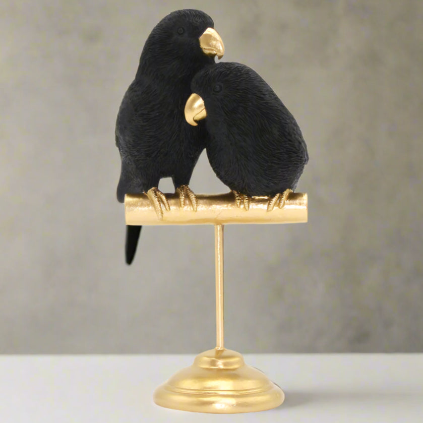 Two black birds on a gold stand against a white background