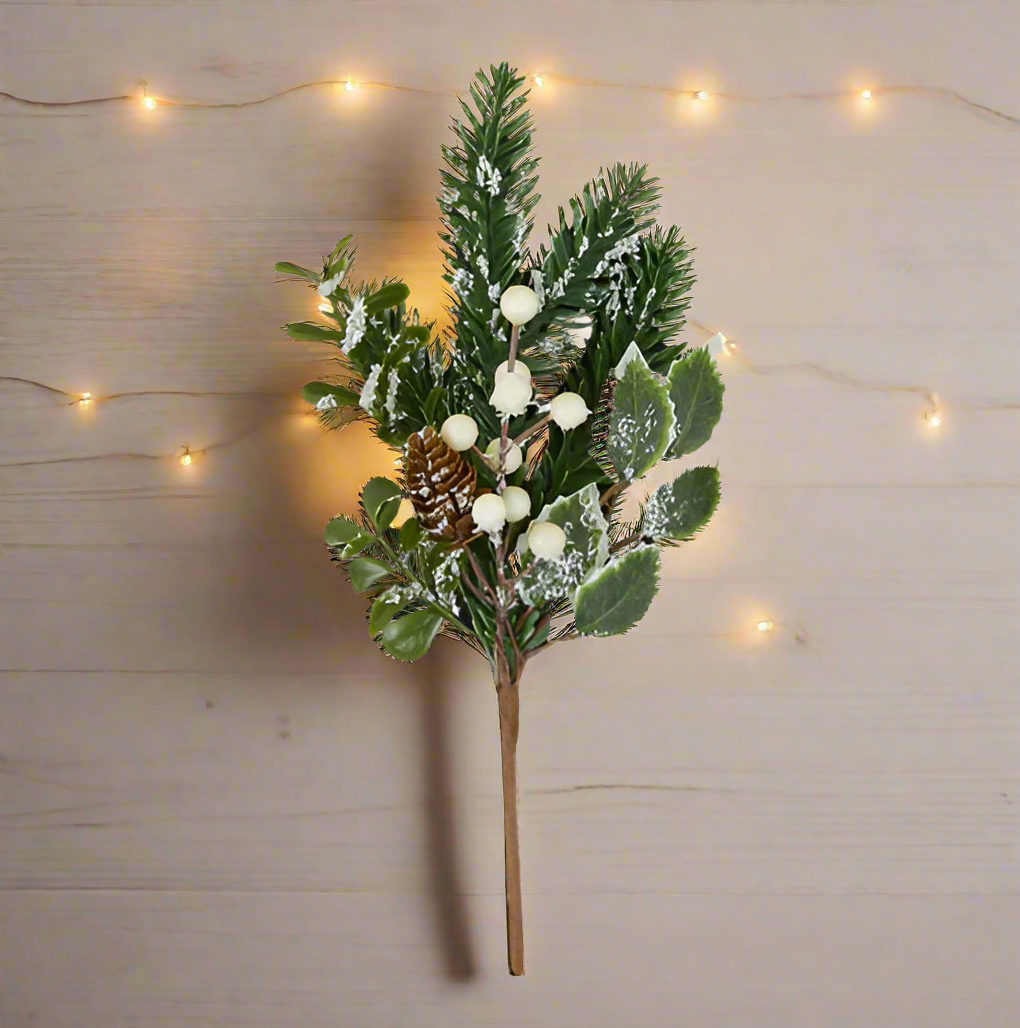 Artificial Christmas branch with green leaves, white berries, and a pine cone on a white background