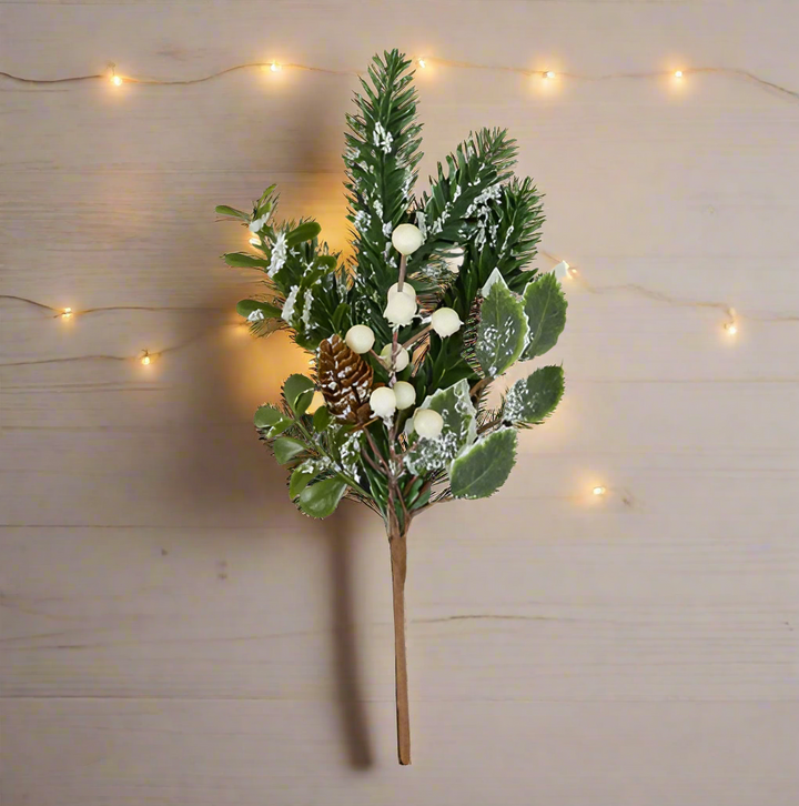 Artificial Christmas branch with green leaves, white berries, and a pine cone on a white background