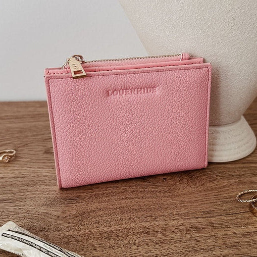 Pink louenhide wallet on a wooden surface with rings and a tube of lip balm.