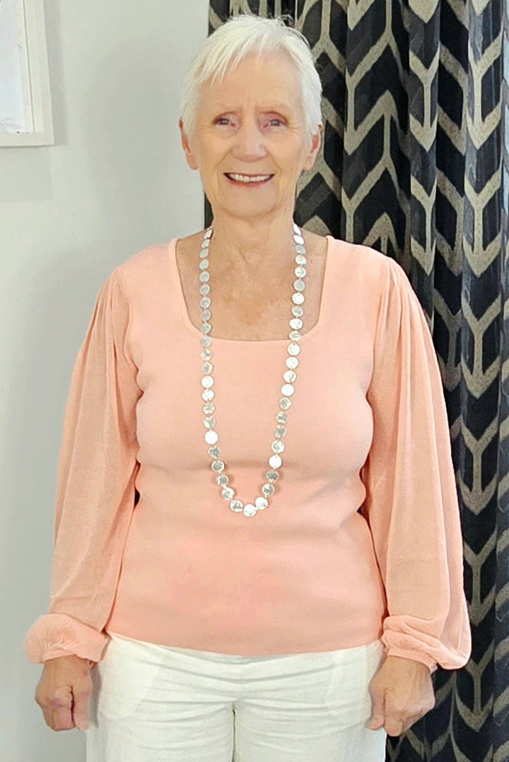 Woman wearing a pink top and white pants standing in a room with a patterned curtain.