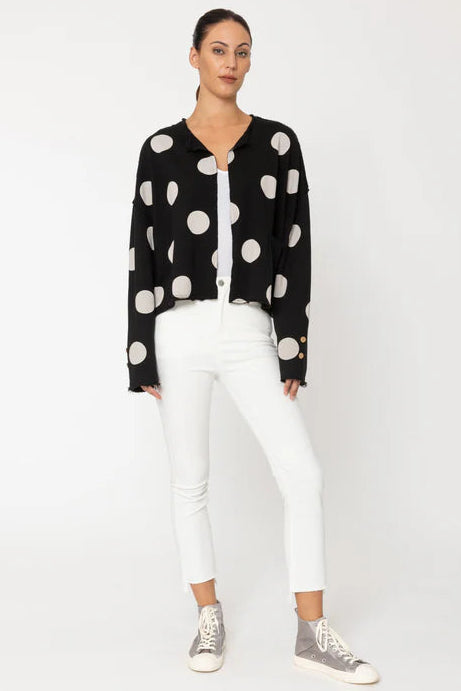 Woman wearing a black polka dot cardigan, white pants, and sneakers on a white background