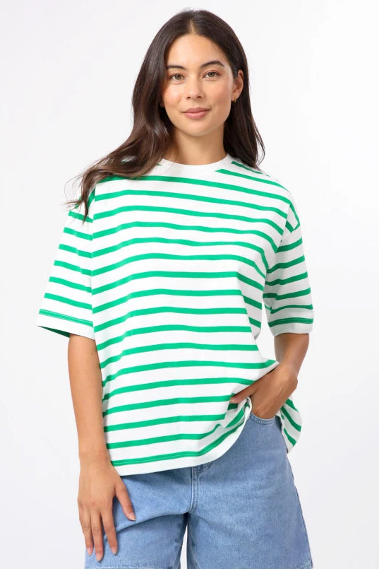 A woman modeling a green and white horizontally striped short-sleeve t-shirt with light-wash denim shorts, set against a plain white studio background.