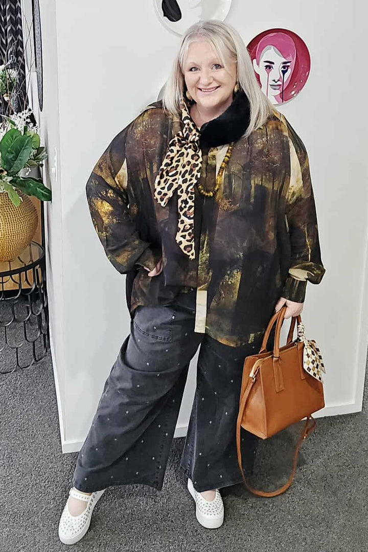 Woman in stylish outfit with patterned coat and leopard print top, holding a brown handbag.