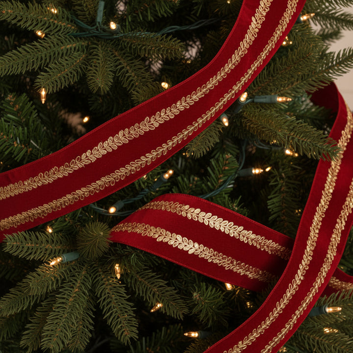 A roll of deep red velvet ribbon with two parallel gold metallic laurel leaf borders, shown unrolled on a clean white background.