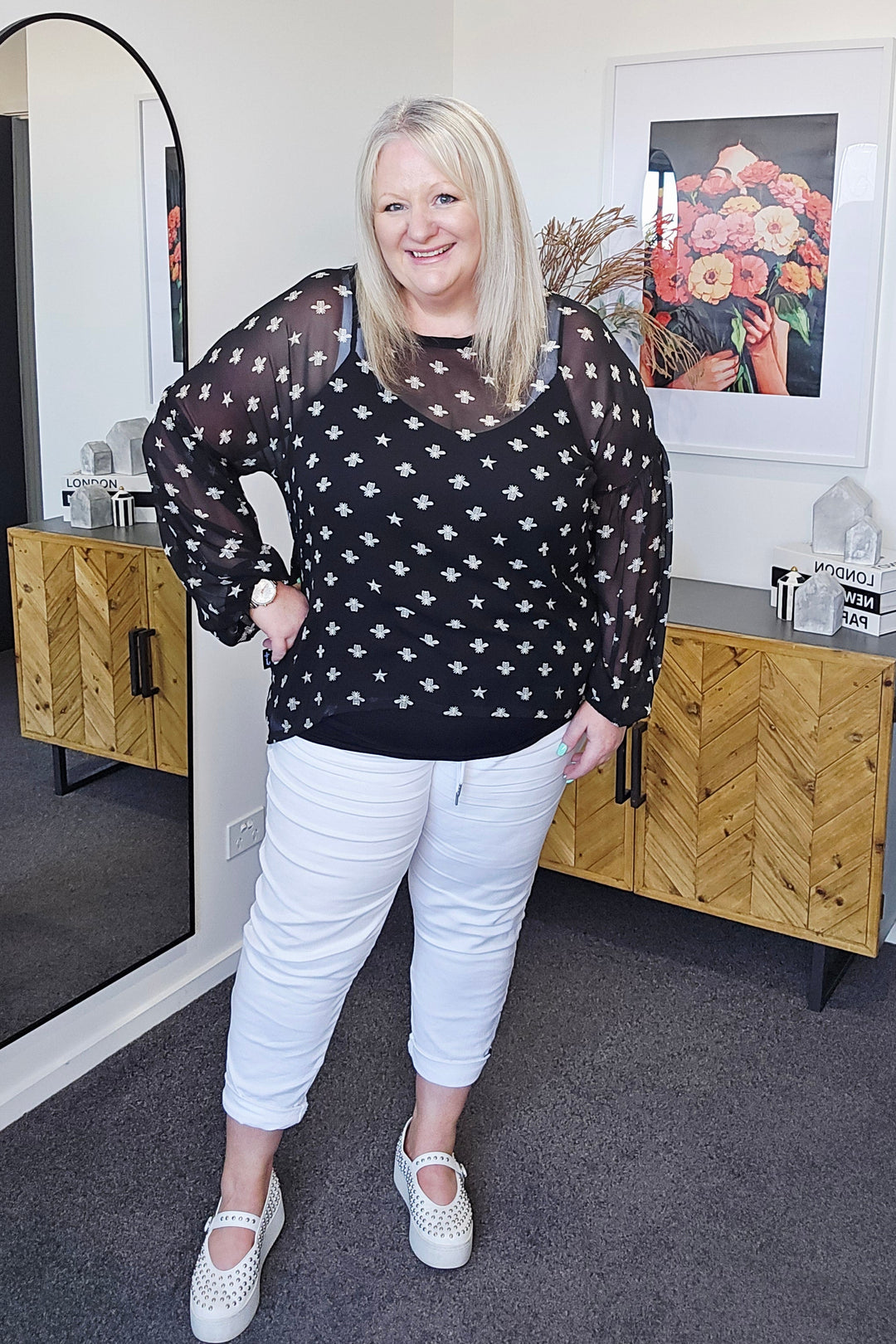 Person standing in a room with a desk, chair, and decorative items.
