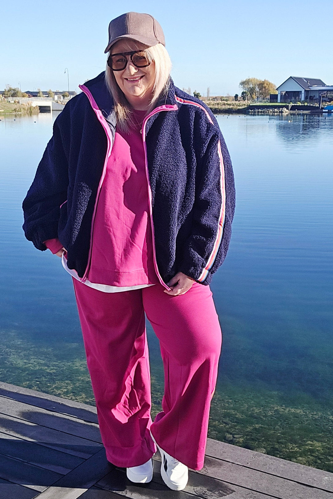 Person in pink pants and dark jacket standing on a wooden deck with a scenic background