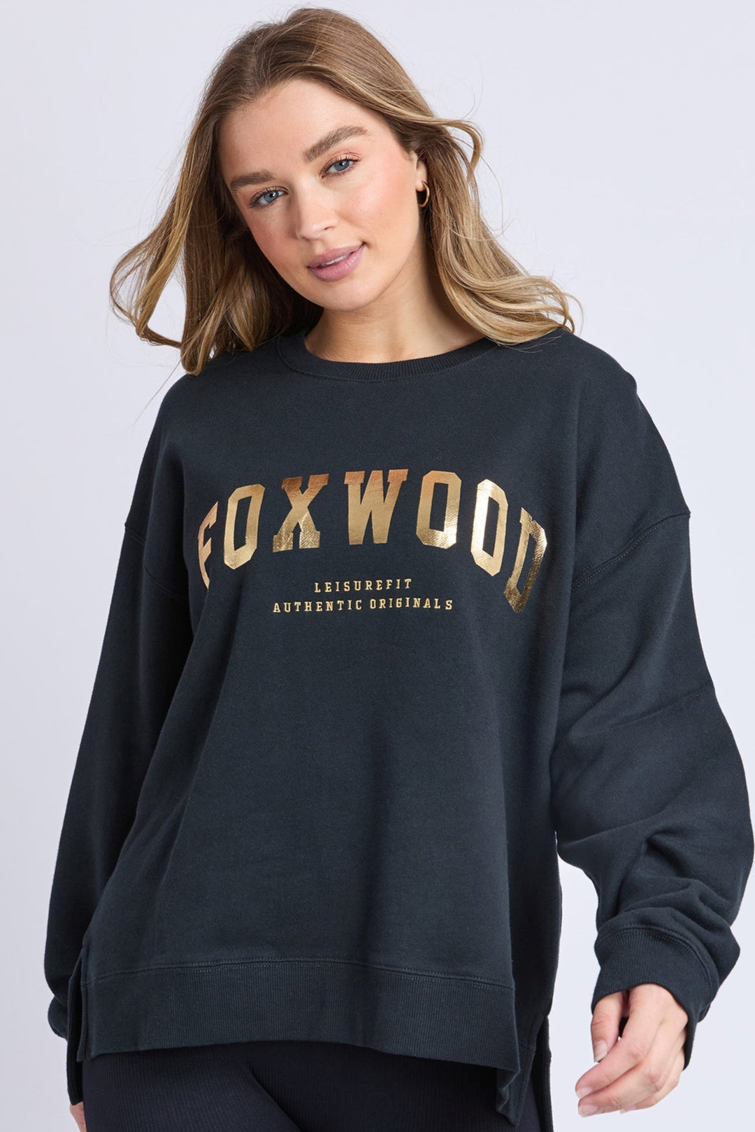 Woman wearing a black sweatshirt with 'FOXWOOD' printed in gold on a light gray background