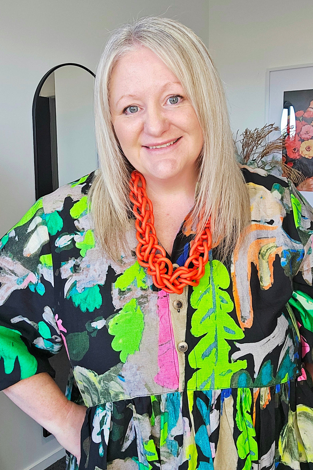 Woman wearing a colorful dress with a pattern of green leaves and black background, standing indoors.