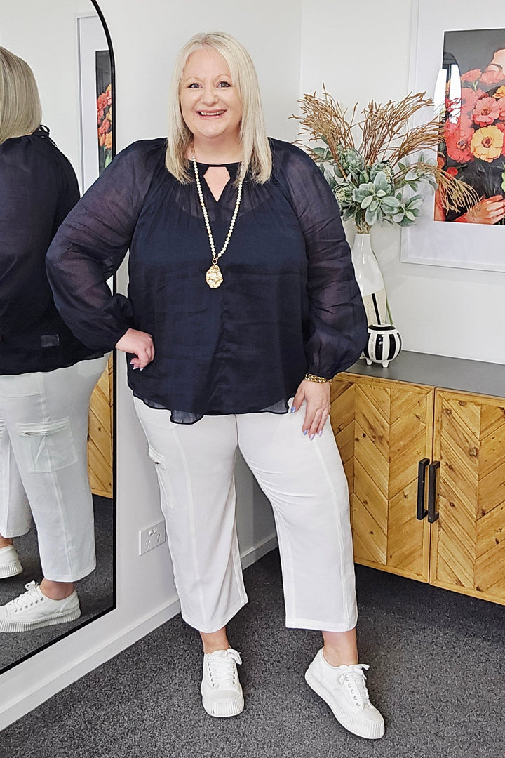 Woman standing in front of a mirror with a floral arrangement on the wall.