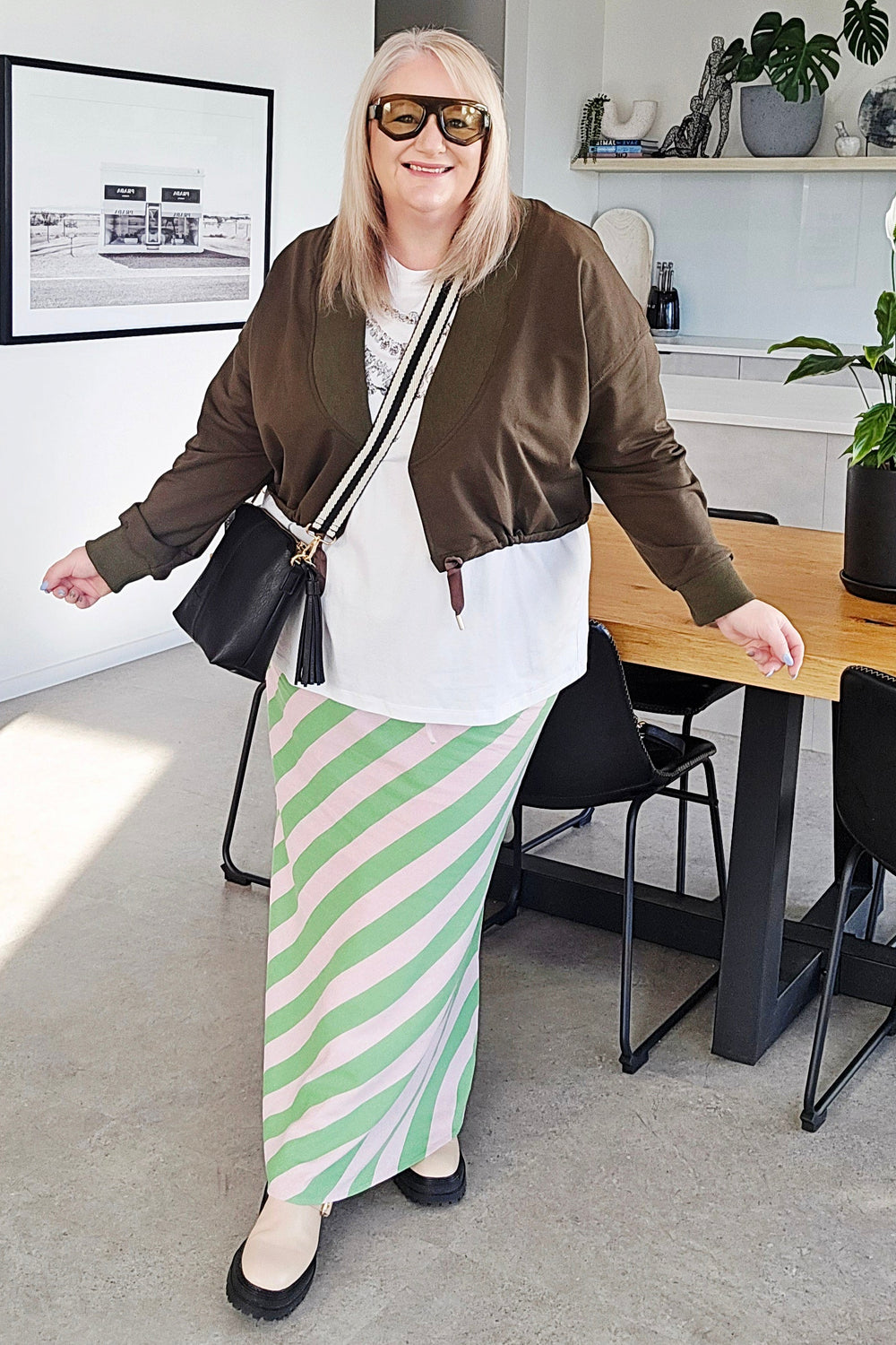 Woman in a stylish outfit with a green and white striped skirt in a modern home setting.