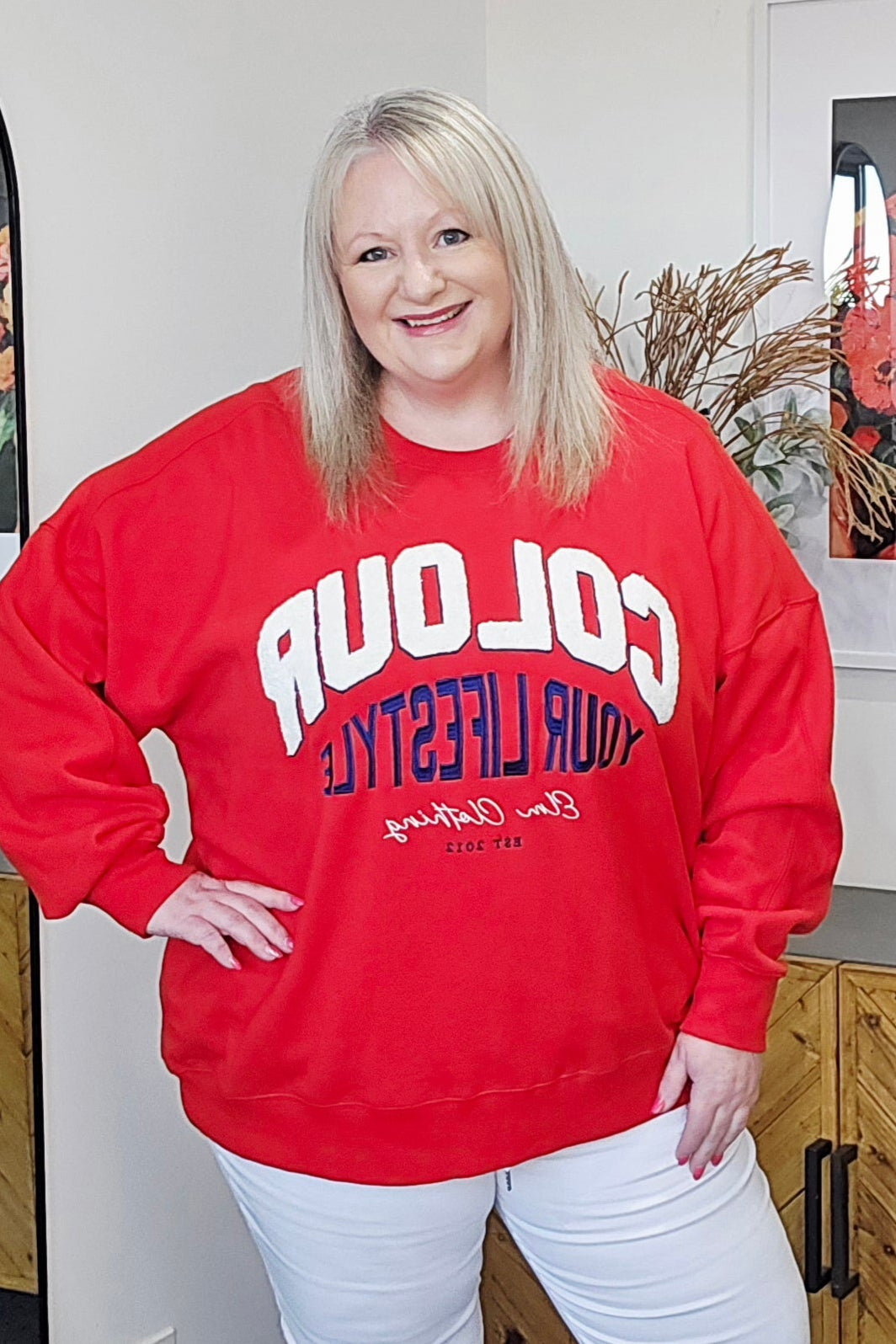 Person wearing a red sweatshirt with text in a room with wooden furniture and decorative items.