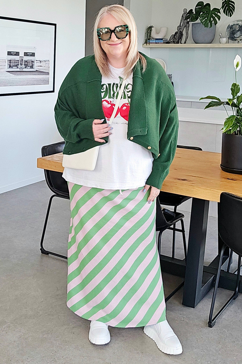Person wearing a green jacket and striped skirt in a modern living room.