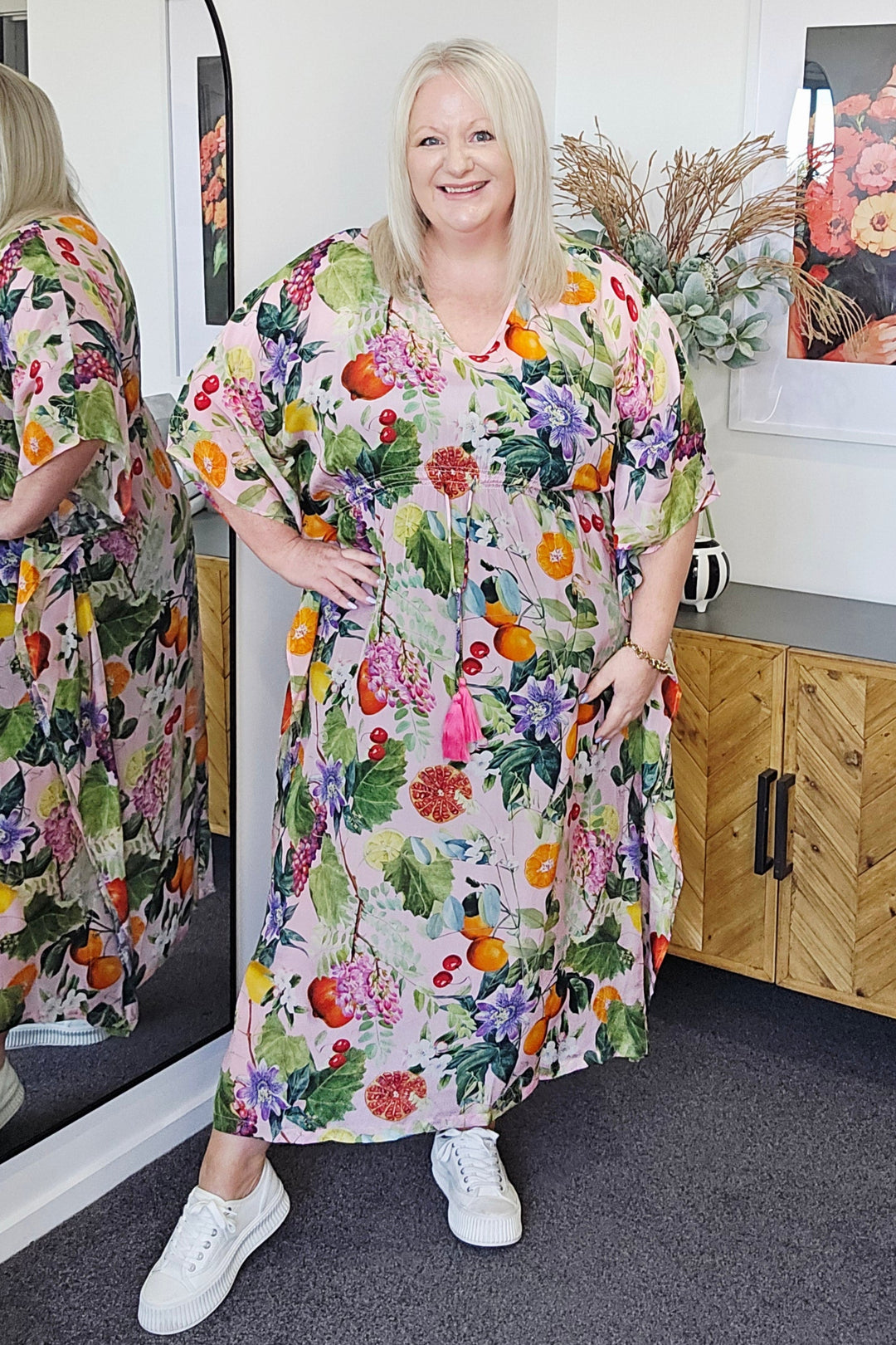 Woman standing next to a table with a Seduce Sonya fruitsy dress on in a room.