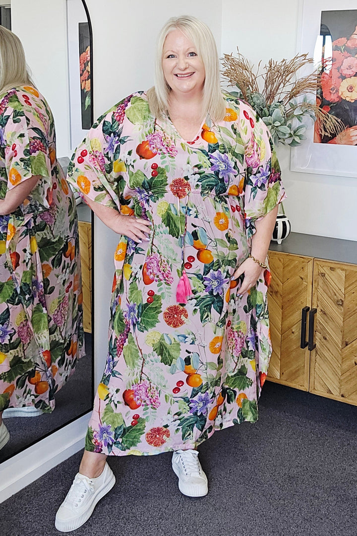 Woman standing next to a table with a Seduce Sonya fruitsy dress on in a room.