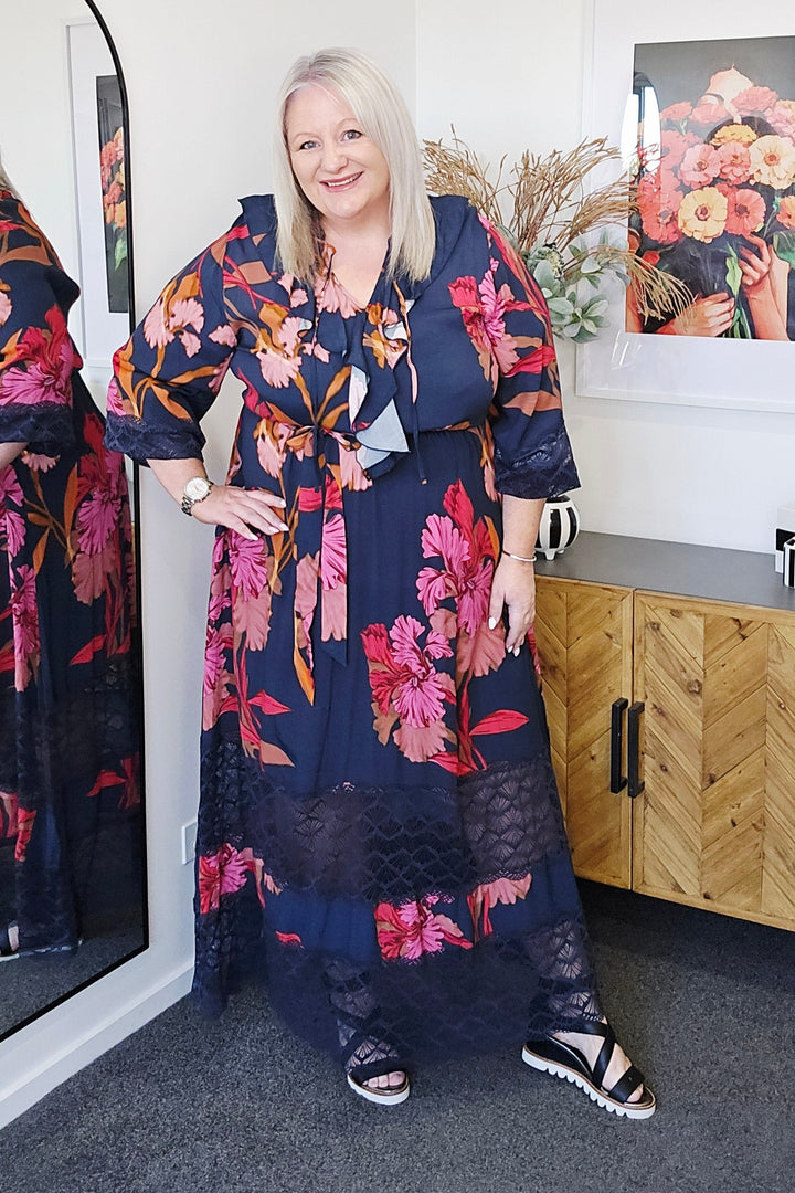 Plus size woman wearing a floral fate & becker dress lying on a gray floor with a wooden box and a magazine in the background.