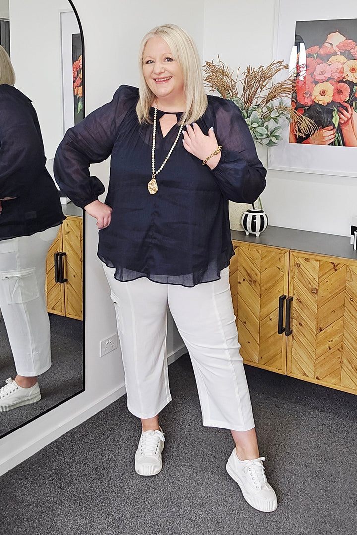 Woman standing in a room with a mirror reflecting her image, holding a plant.