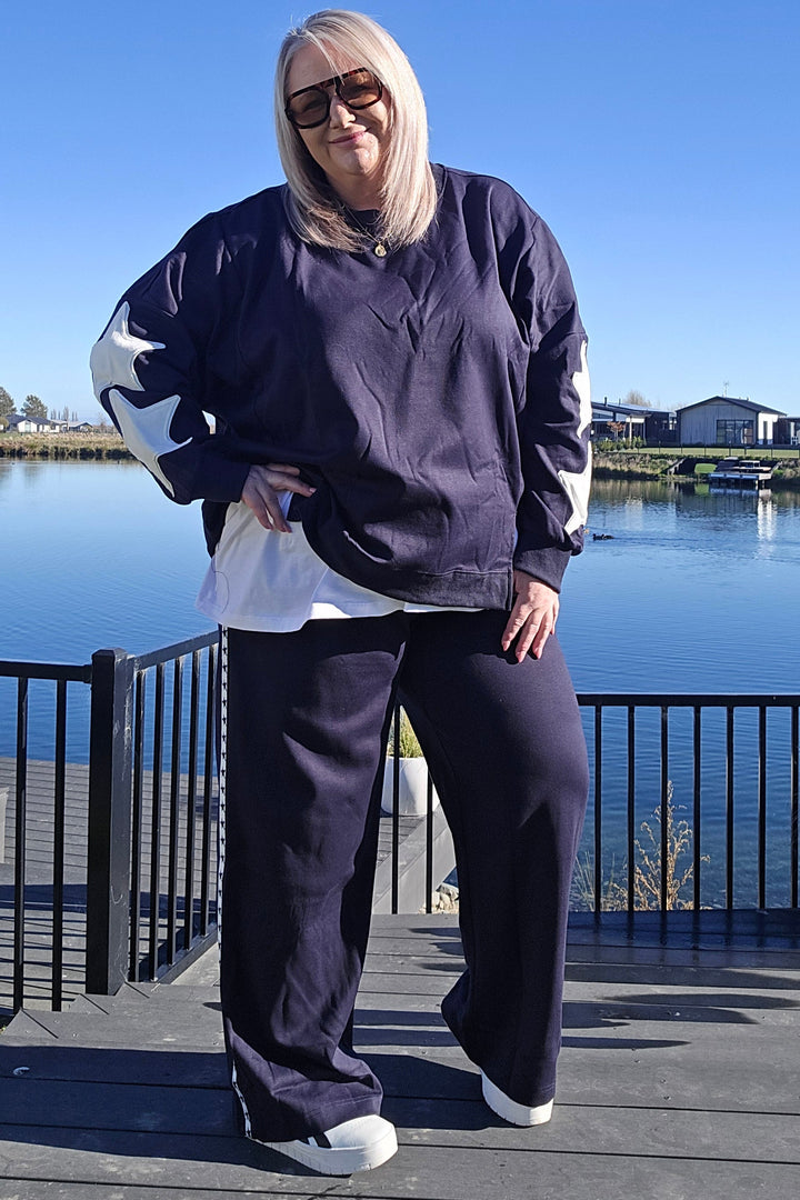 Person wearing a navy tracksuit with white shoes against a blue sky.