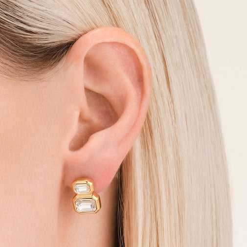 Gold hoop earrings worn by a person with blonde hair on a neutral background