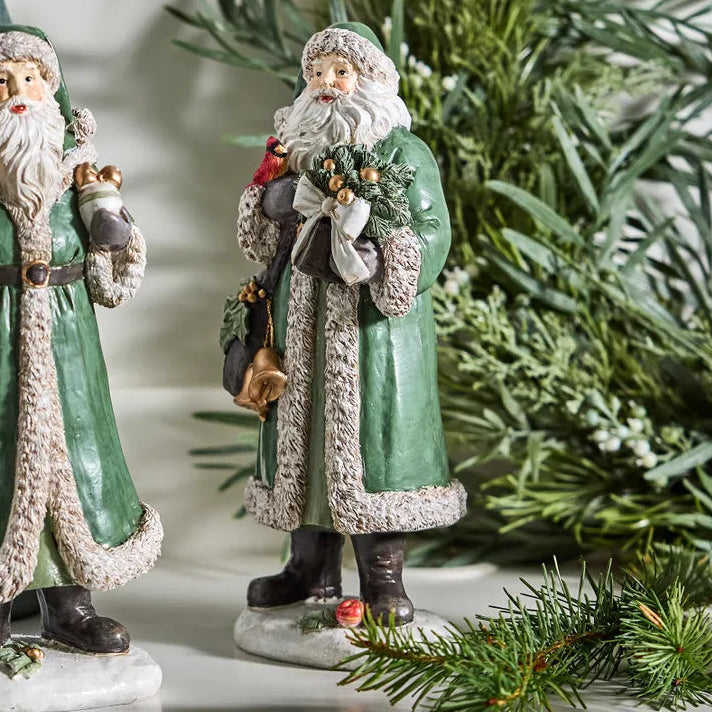 Two decorative Santa Claus figures with green robes and white beards, standing in front of a Christmas tree.